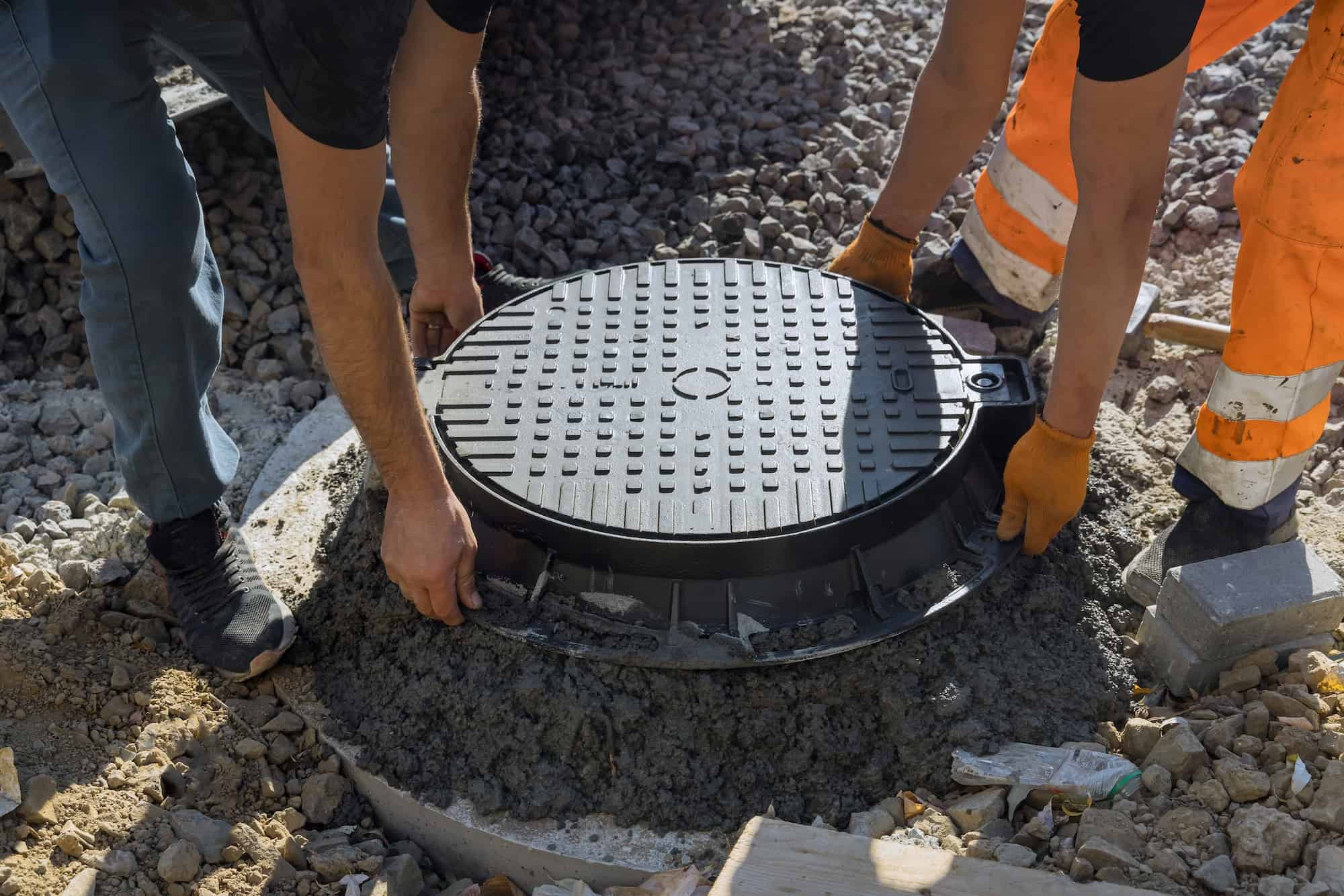 a cast iron sewer hatch is being installed in a concrete well in preparation for the installation